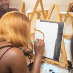 Grupo de adultos participa de uma aula de pintura e trabalha concentrado em projetos artísticos.