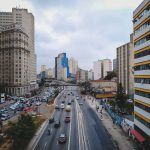 Avenida urbana com carros circulando entre edifícios modernos.