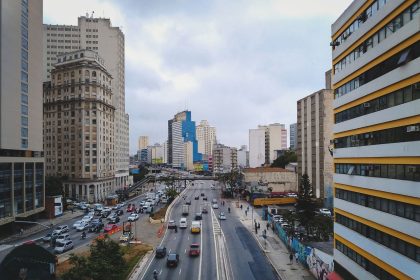 Avenida urbana com carros circulando entre edifícios modernos.