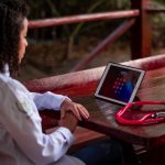 Profissional de saúde usando um tablet e segurando um estetoscópio em uma área externa.