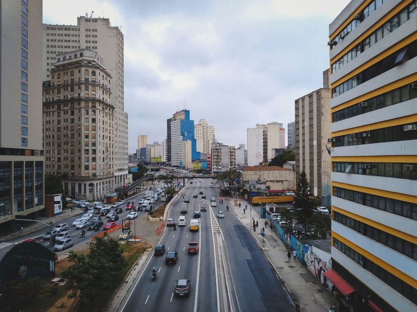 Avenida urbana com carros circulando entre edifícios modernos.