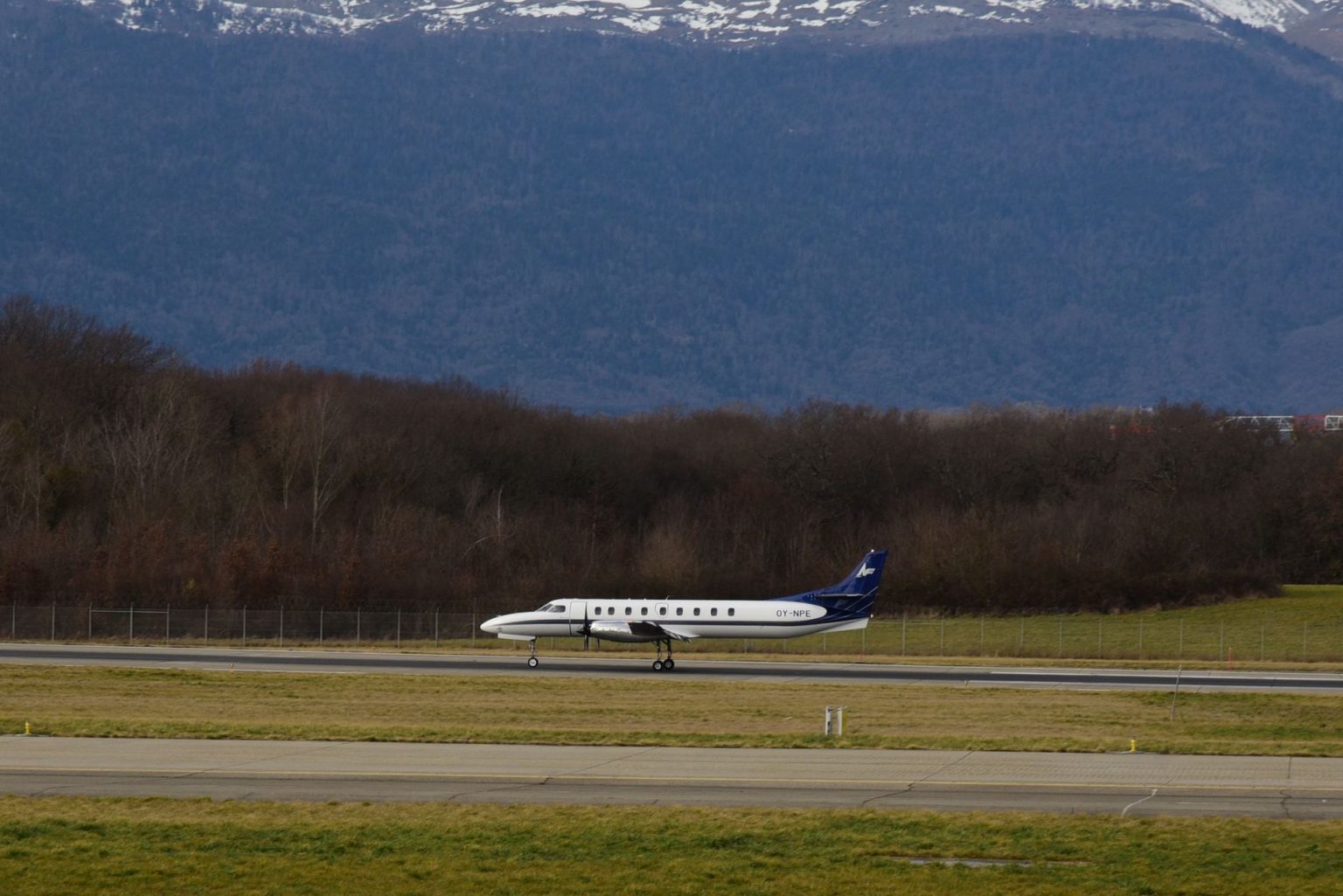 Avião de passageiros taxiando na pista de um aeroporto, com montanhas ao fundo.