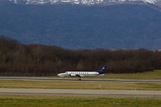 Avião de passageiros taxiando na pista de um aeroporto, com montanhas ao fundo.