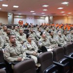 Bombeiros uniformizados participam de uma conferência de treinamento para atendimento a emergências em ambiente interno.