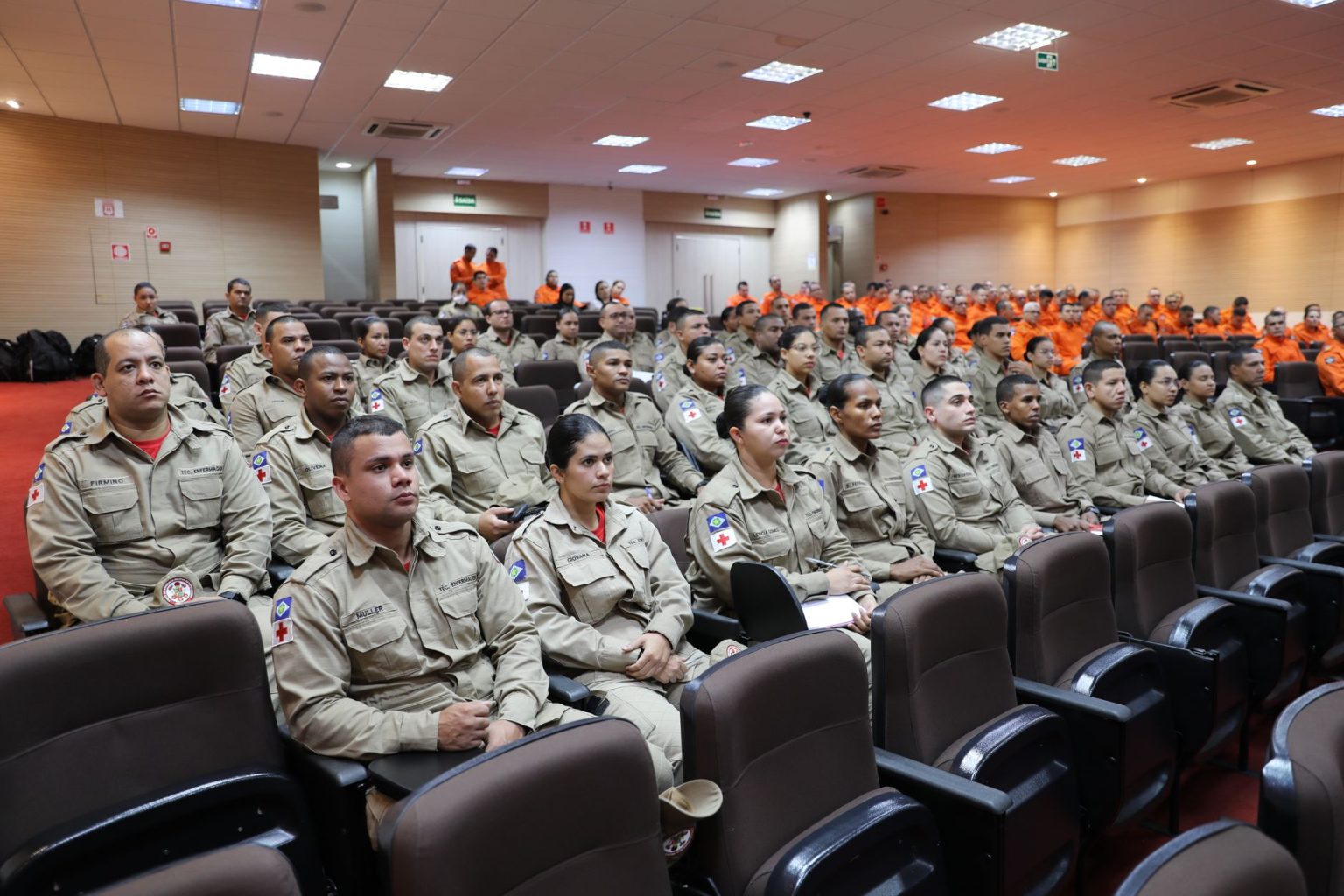 Bombeiros uniformizados participam de uma conferência de treinamento para atendimento a emergências em ambiente interno.