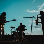 Banda se apresenta ao ar livre durante o pôr do sol, diante do público.