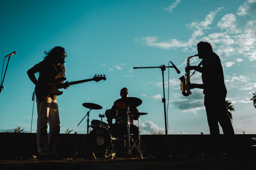 Banda se apresenta ao ar livre durante o pôr do sol, diante do público.